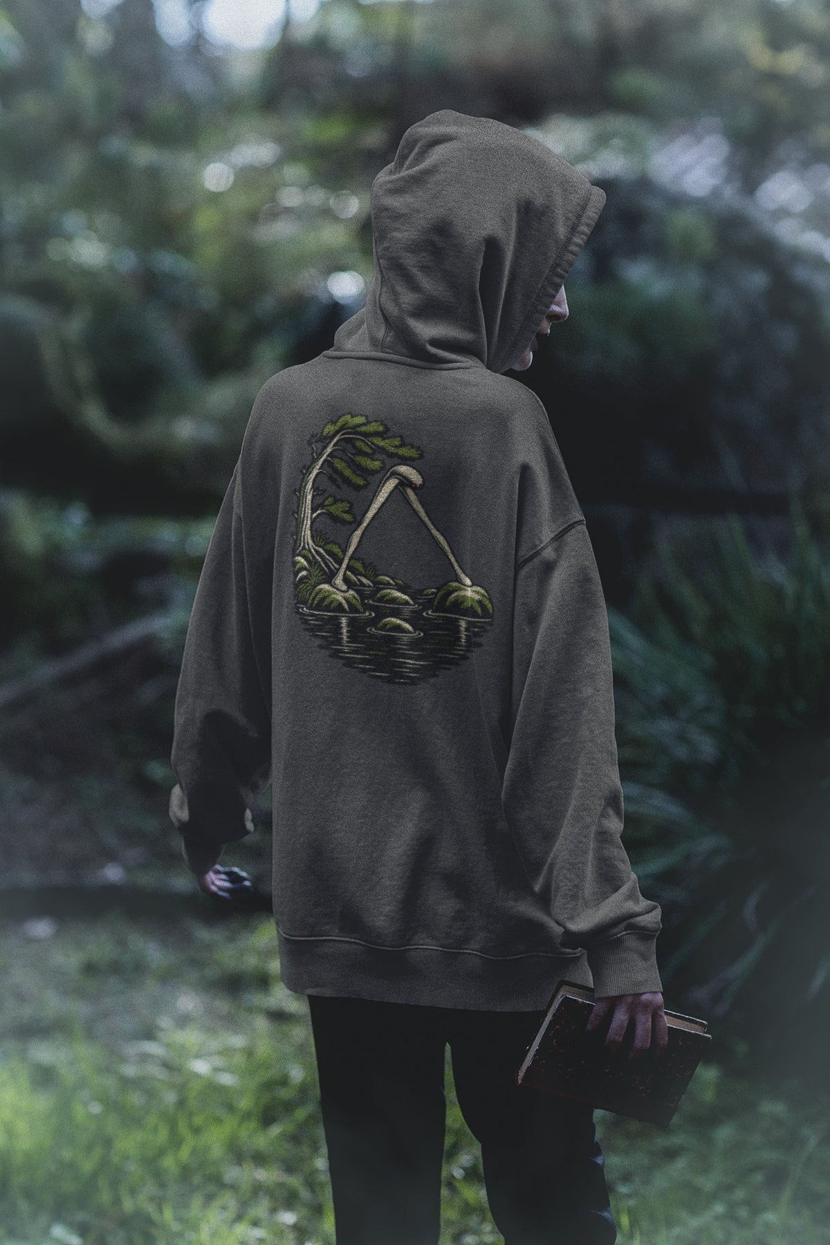 Small Hours Zip Hoodie in Dark Heather, worn by a woman seen from behind in a dark forest, showing the large print on the back. Digital product mockup.
