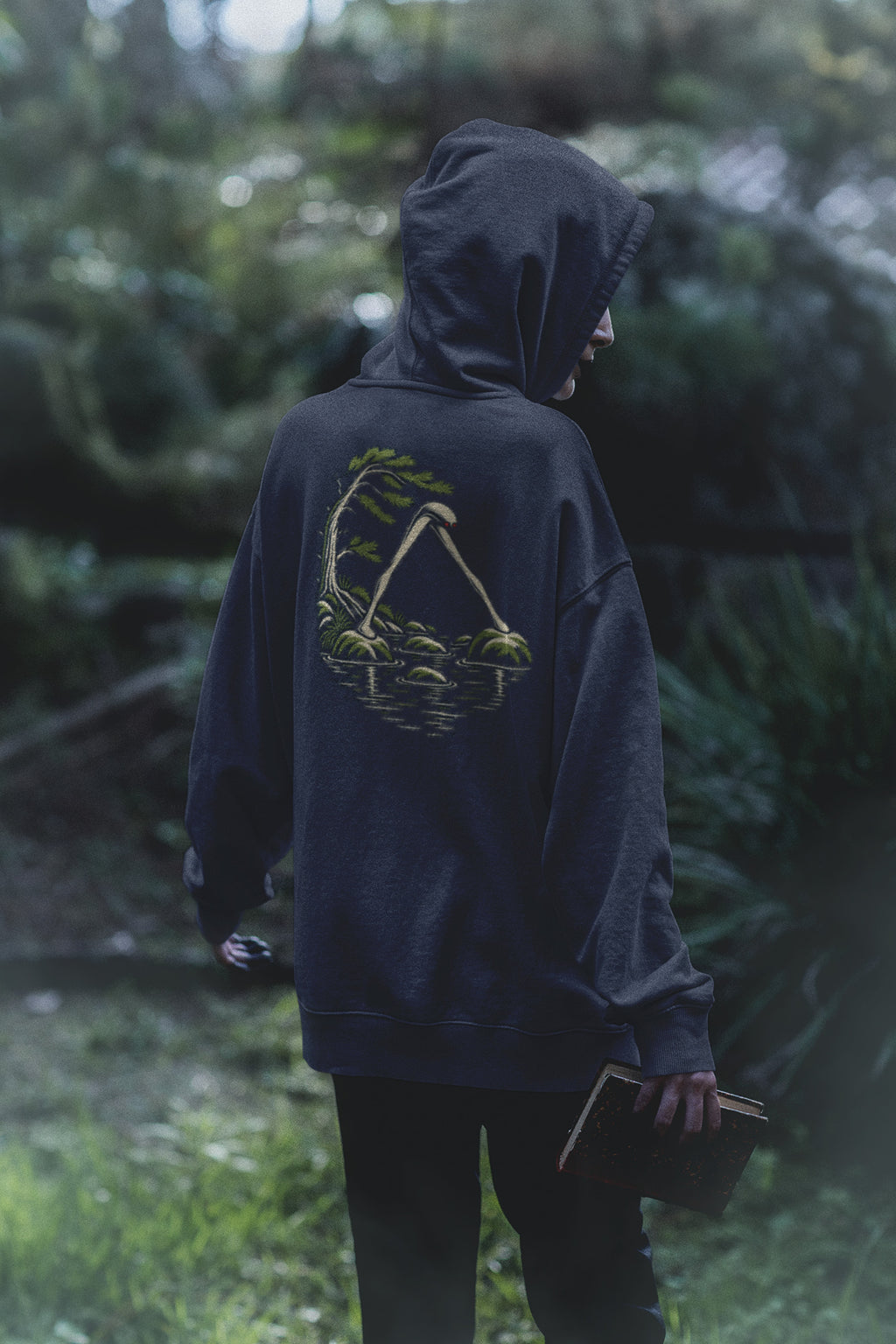 Small Hours Zip Hoodie in Navy, worn by a woman seen from behind in a dark forest, showing the large print on the back. Digital product mockup.