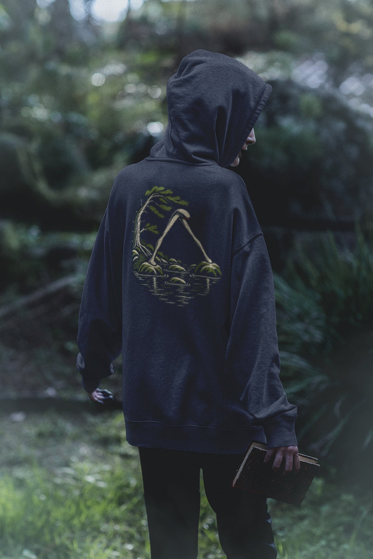 Small Hours Zip Hoodie in Navy, worn by a woman seen from behind in a dark forest, showing the large print on the back. Digital product mockup.