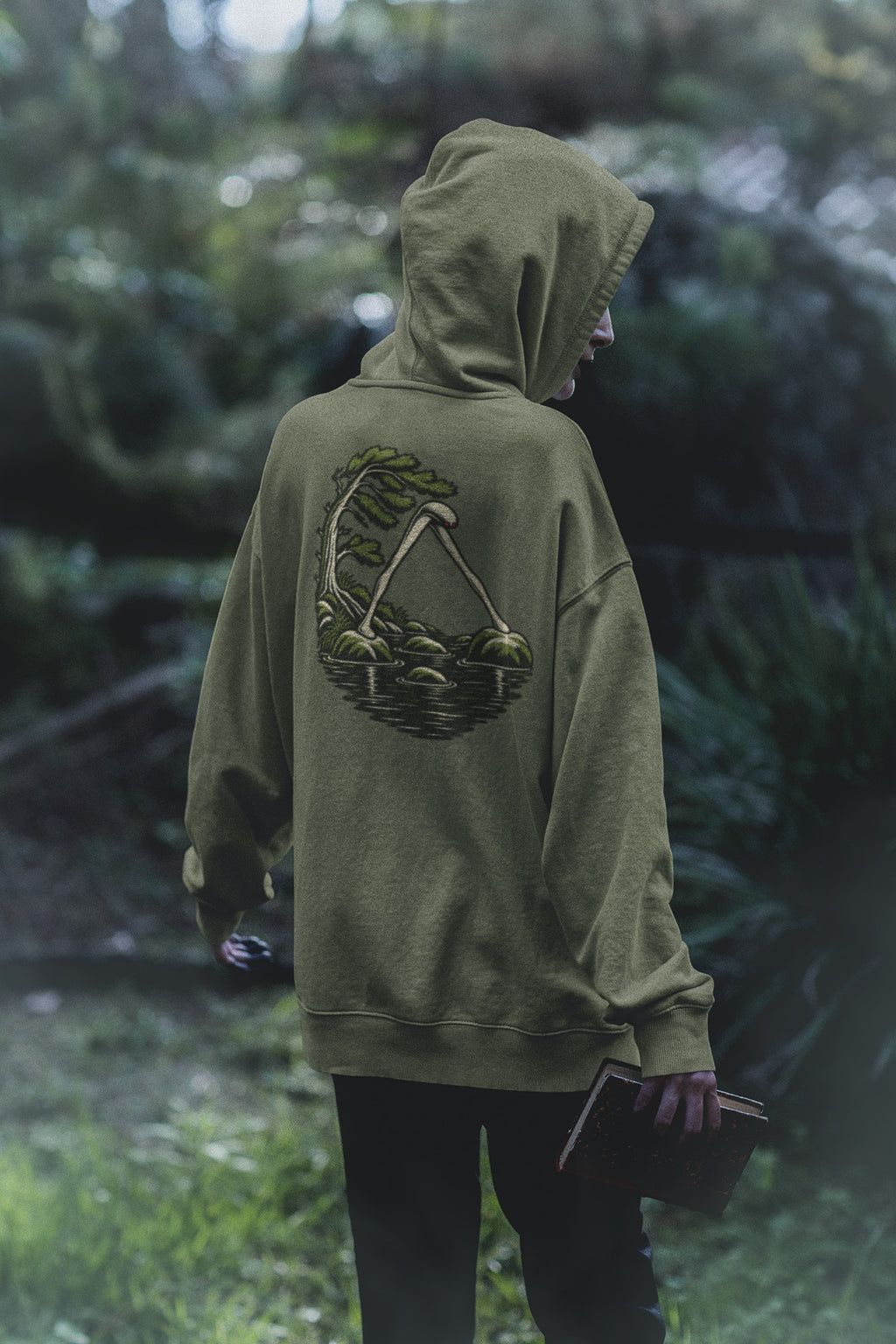 Small Hours Zip Hoodie in Military Green, worn by a woman seen from behind in a dark forest, showing the large print on the back. Digital product mockup.
