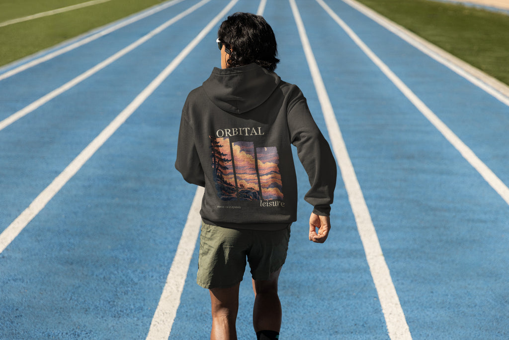 Edge of Evening Zip Hoodie in Black, worn by a man seen from behind on a running track, showing the large print on the back. Digital product mockup.