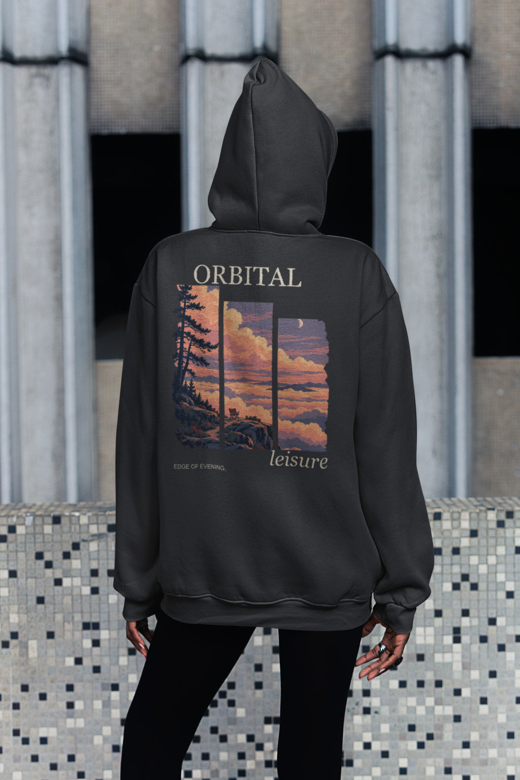 Edge of Evening Zip Hoodie in Black, worn by a woman seen from behind on a city sidewalk, showing the large print on the back. Digital product mockup.