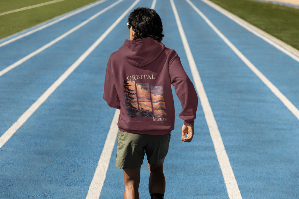 Edge of Evening Zip Hoodie in Maroon, worn by a man seen from behind on a running track, showing the large print on the back. Digital product mockup.