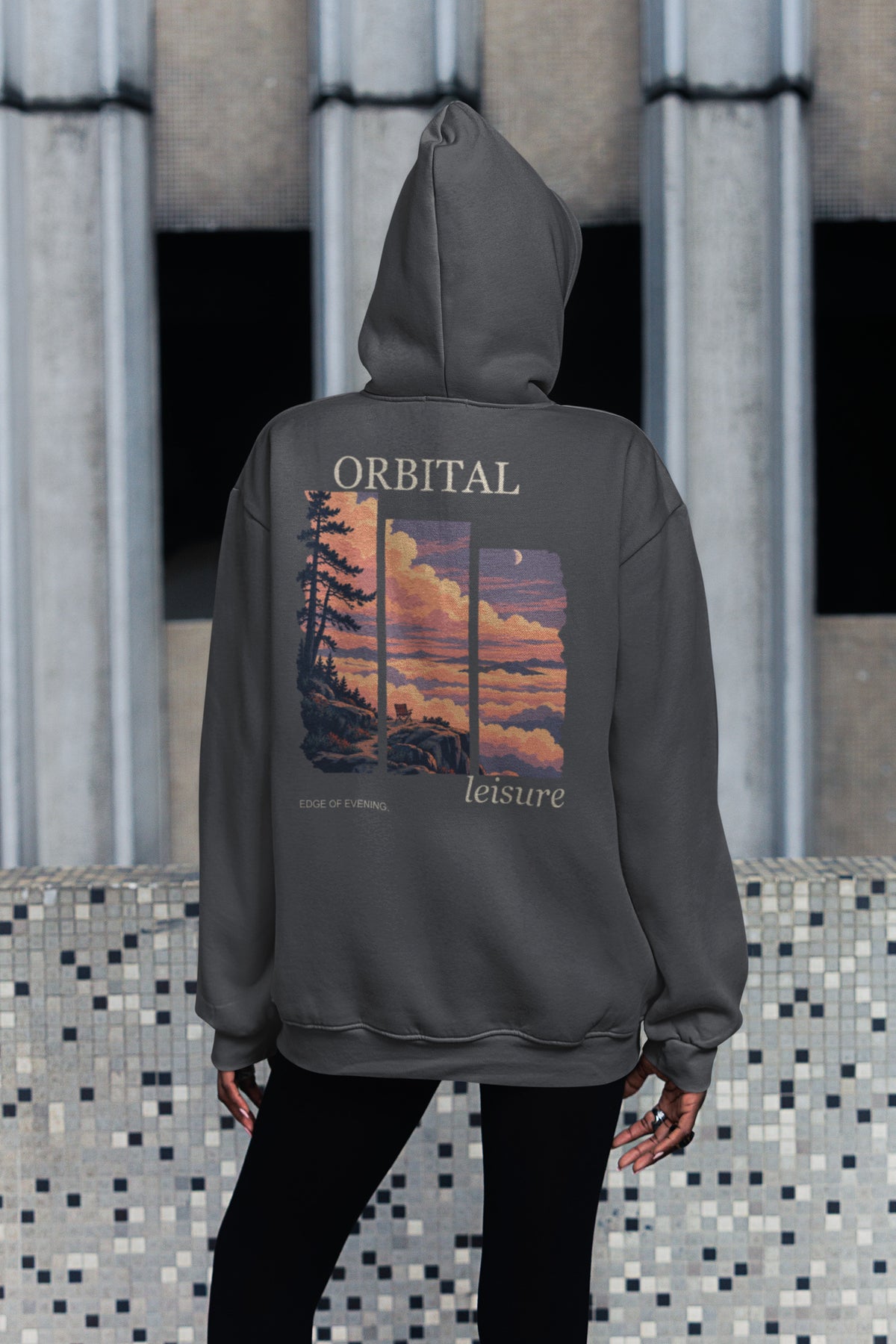 Edge of Evening Zip Hoodie in Dark Heather, worn by a woman seen from behind on a city sidewalk, showing the large print on the back. Digital product mockup.