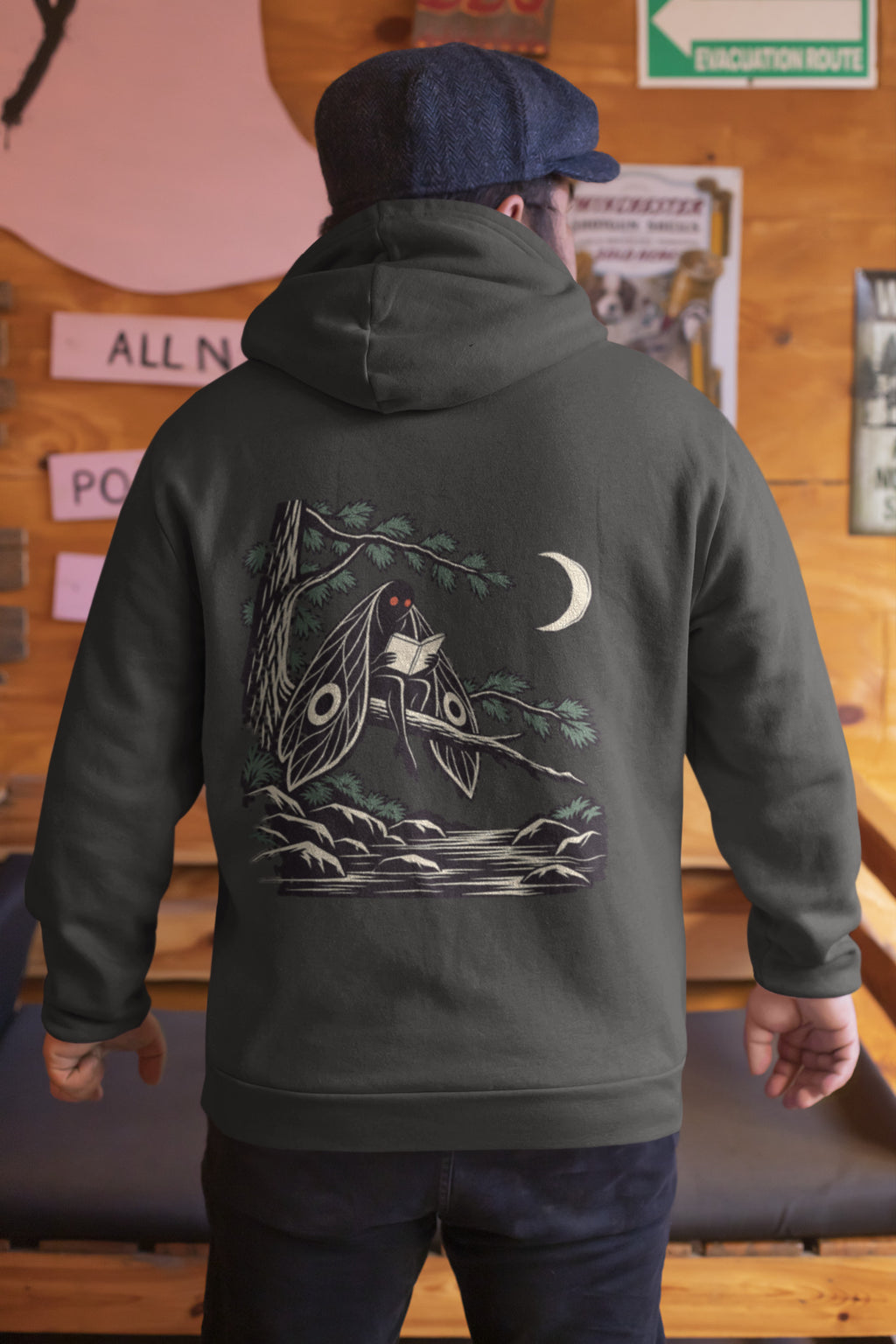 Night Library Zip Hoodie in Black, worn by a man seen from behind in a wood-panelled bar, showing the large print on the back. Digital product mockup.