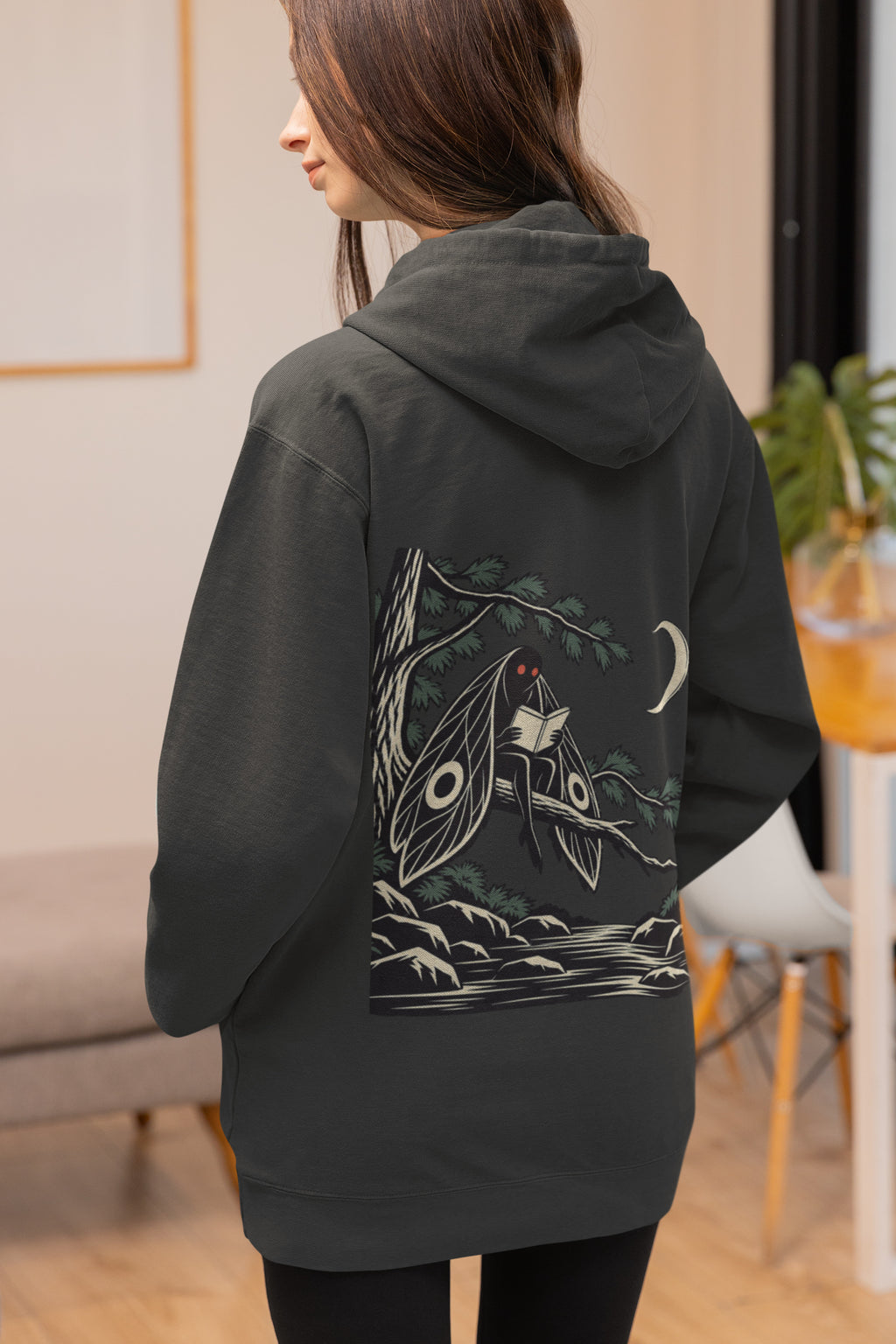Night Library Zip Hoodie in Black, worn by a woman seen from behind at home, showing the large print on the back. Digital product mockup.