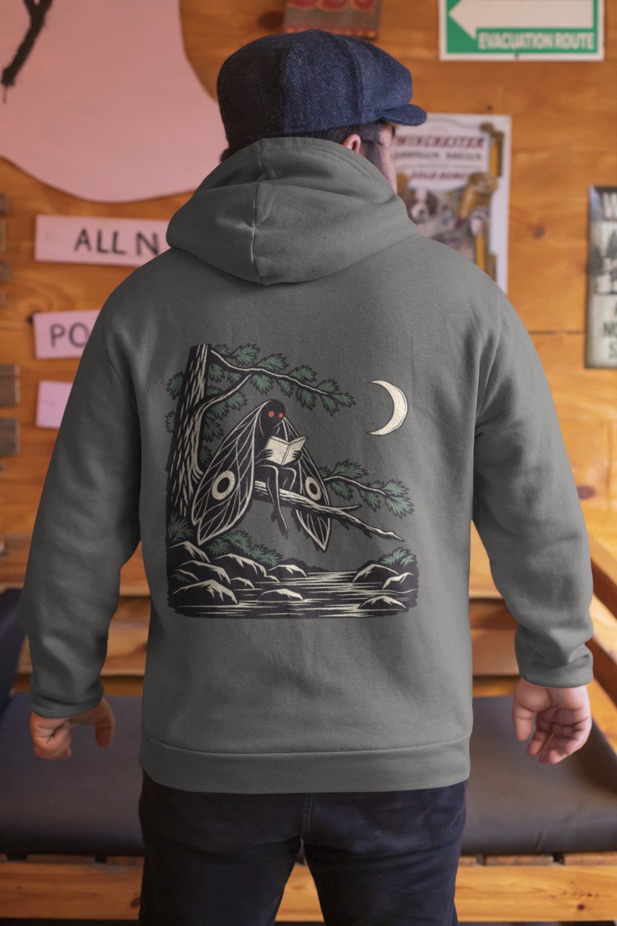 Night Library Zip Hoodie in Dark Heather, worn by a man seen from behind in a wood-panelled bar, showing the large print on the back. Digital product mockup.