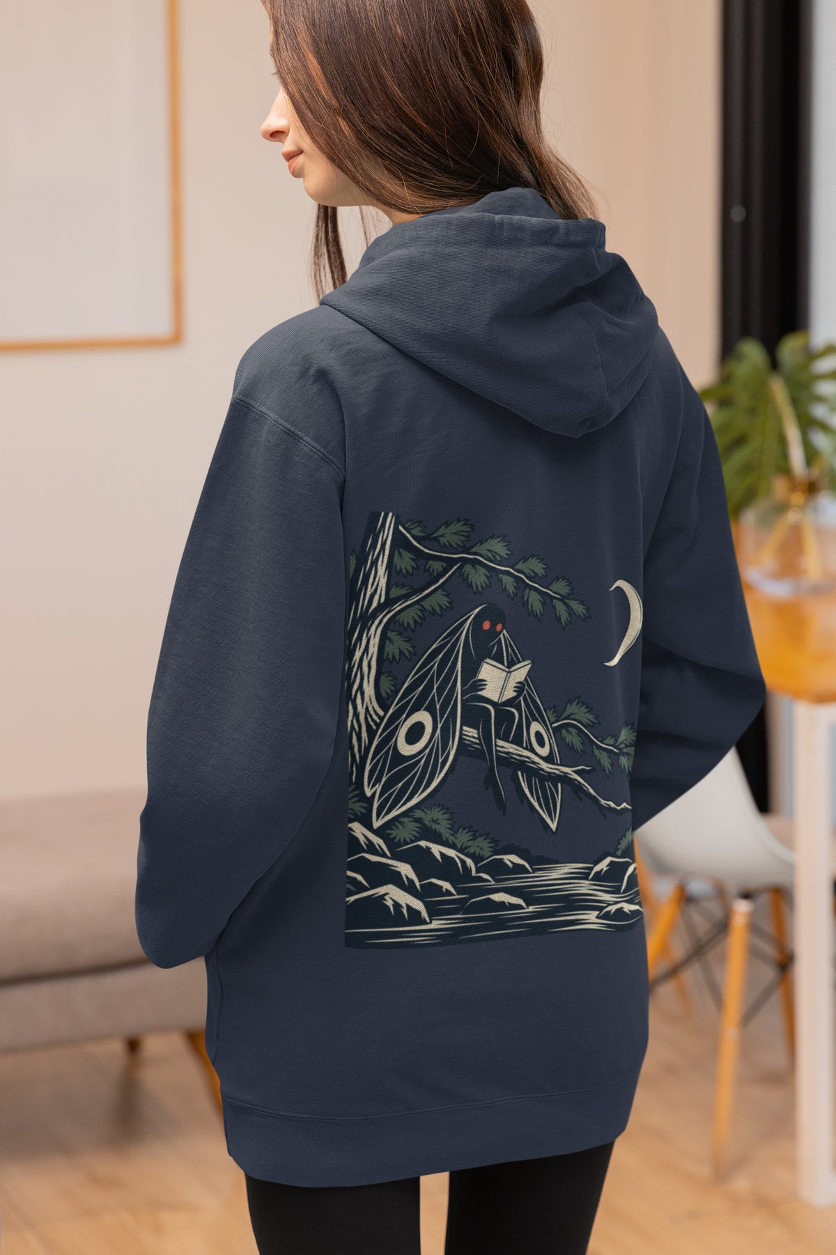 Night Library Zip Hoodie in Navy, worn by a woman seen from behind at home, showing the large print on the back. Digital product mockup.