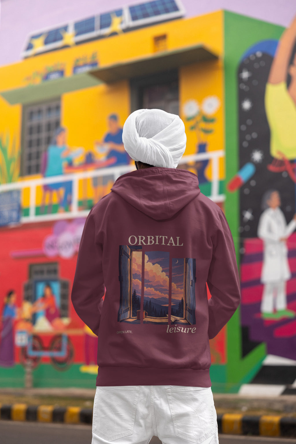Open Late Zip Hoodie in Maroon, worn by a man seen from behind in a turban by a painted mural, showing the large print on the back. Digital product mockup.