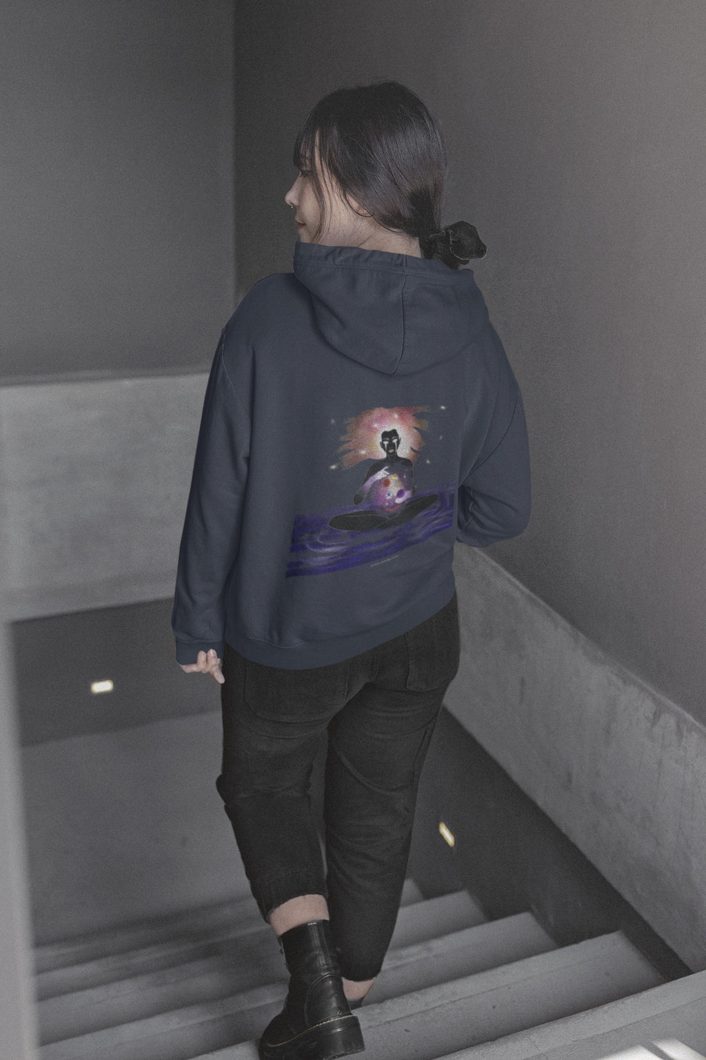 Orbit Keeper Zip Hoodie in Navy, worn by a woman seen from behind walking down a staircase, showing the large print on the back. Digital product mockup.