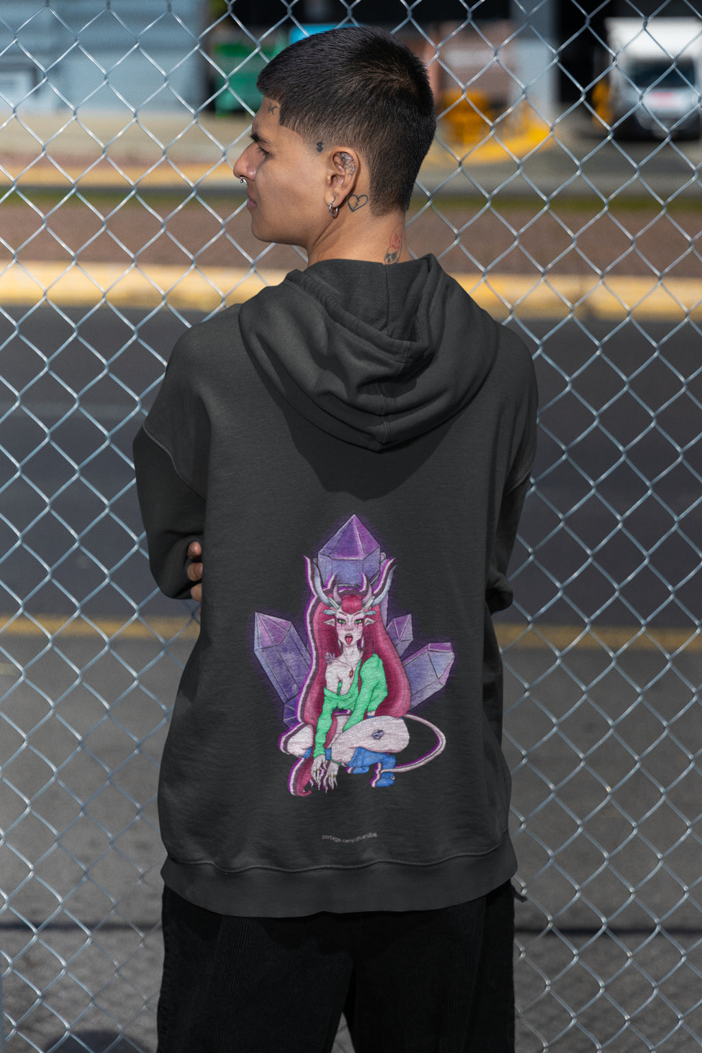 Amethyst After Hours Zip Hoodie in Black, worn by a man seen from behind by a chain-link fence, showing the large print on the back. Digital product mockup.