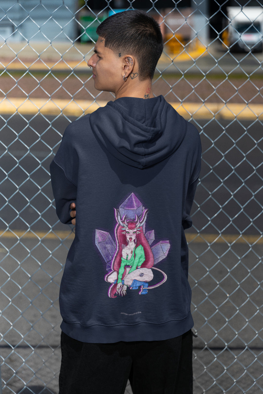 Amethyst After Hours Zip Hoodie in Navy, worn by a man seen from behind by a chain-link fence, showing the large print on the back. Digital product mockup.