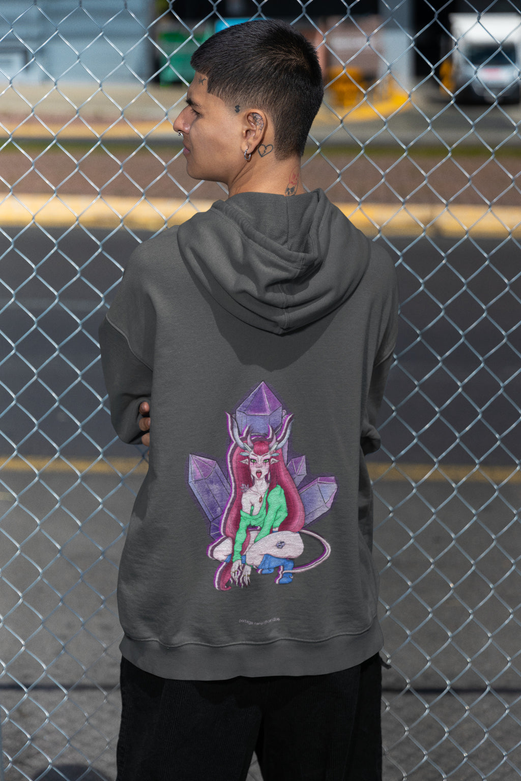 Amethyst After Hours Zip Hoodie in Dark Heather, worn by a man seen from behind by a chain-link fence, showing the large print on the back. Digital product mockup.