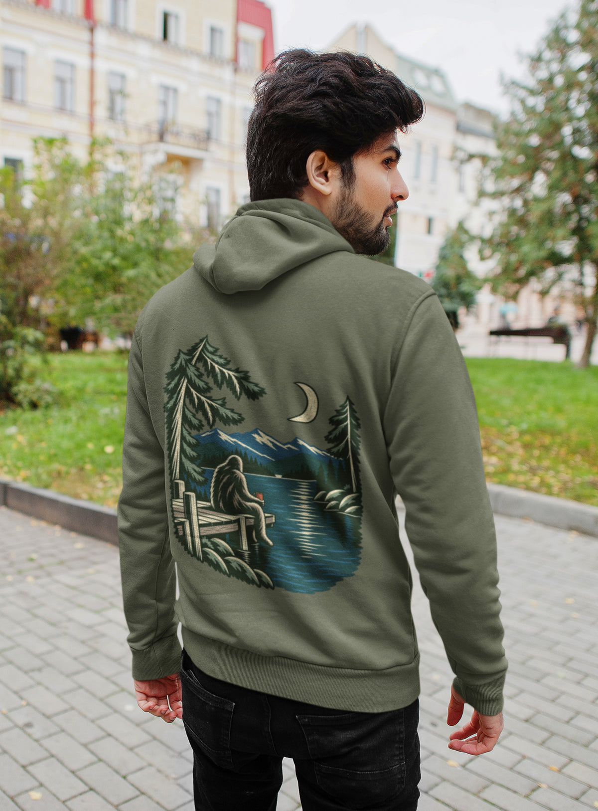Quiet Hours Zip Hoodie in Military Green, worn by a man seen from behind on a quiet city street, showing the large print on the back. Digital product mockup.