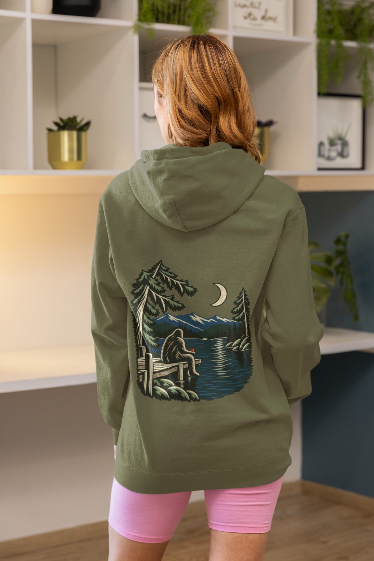 Quiet Hours Zip Hoodie in Military Green, worn by a woman seen from behind at home, showing the large print on the back. Digital product mockup.