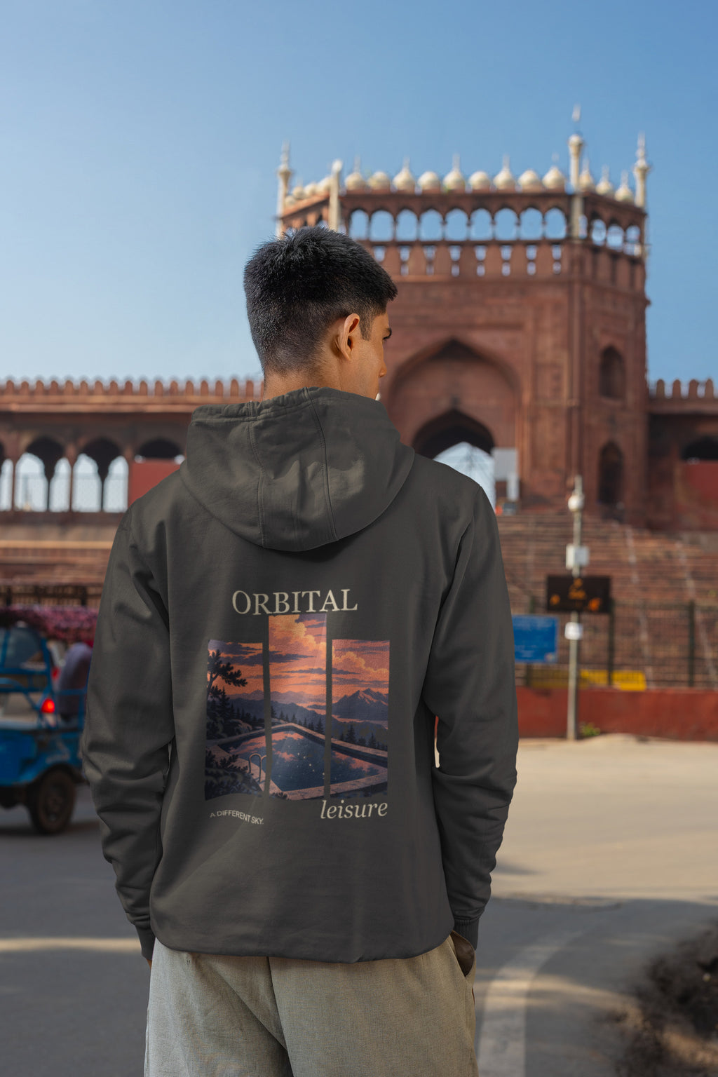 A Different Sky Heavyweight Hoodie in Black, worn by a man seen from behind on a city street, showing the large print on the back. Digital product mockup.