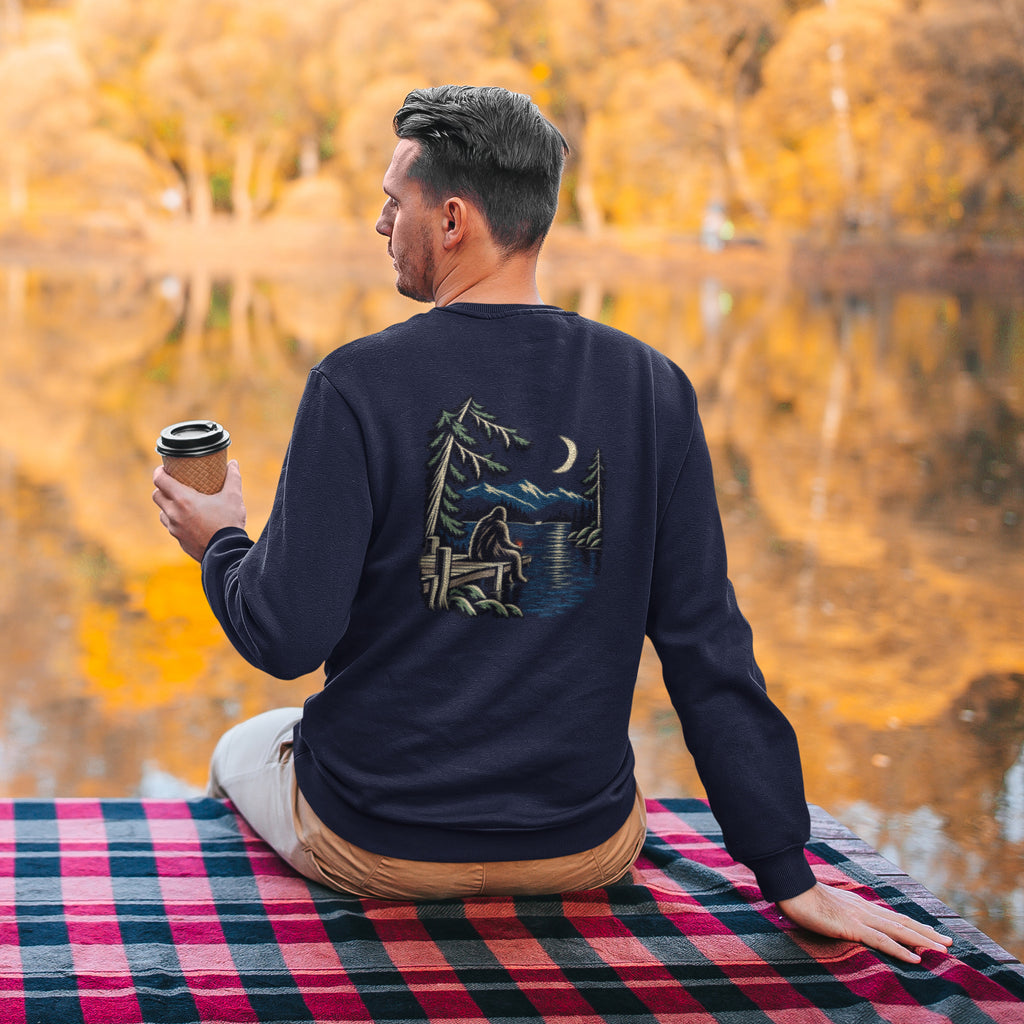 Quiet Hours Garment-Dyed Crewneck in True Navy, worn by a man seen from behind seated by a lake in autumn, showing the large print on the back. Digital product mockup.