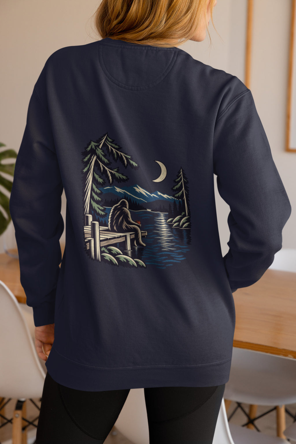 Quiet Hours Garment-Dyed Crewneck in True Navy, worn by a woman seen from behind at home, showing the large print on the back. Digital product mockup.