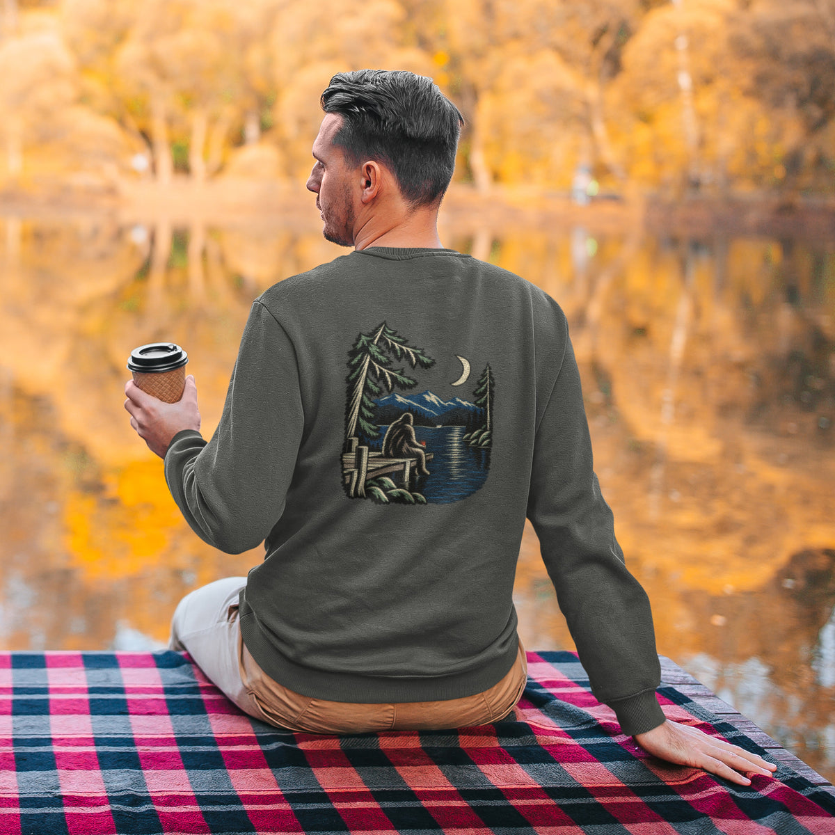 Quiet Hours Garment-Dyed Crewneck in Pepper, worn by a man seen from behind seated by a lake in autumn, showing the large print on the back. Digital product mockup.