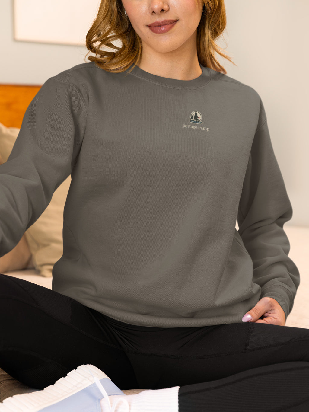Quiet Hours Garment-Dyed Crewneck in Pepper, worn by a woman at home, with the Quiet Hours logo and portage.camp on the chest. Digital product mockup.