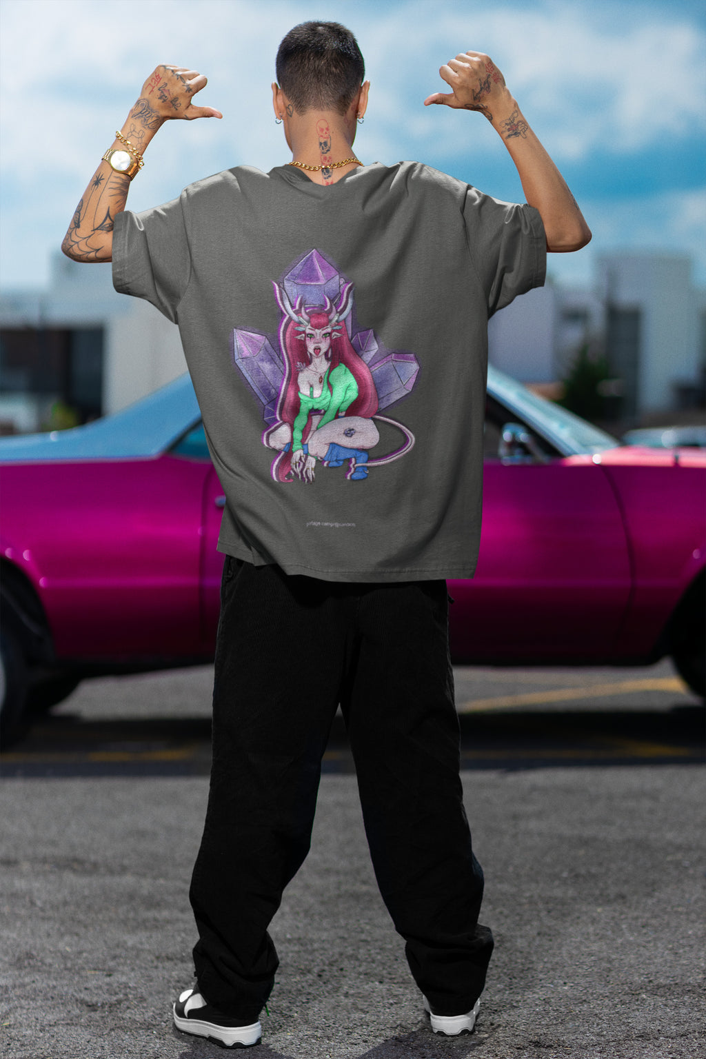Amethyst After Hours Garment-Dyed Tee in Pepper, worn by a man seen from behind by a pink car, showing the large print on the back. Digital product mockup.