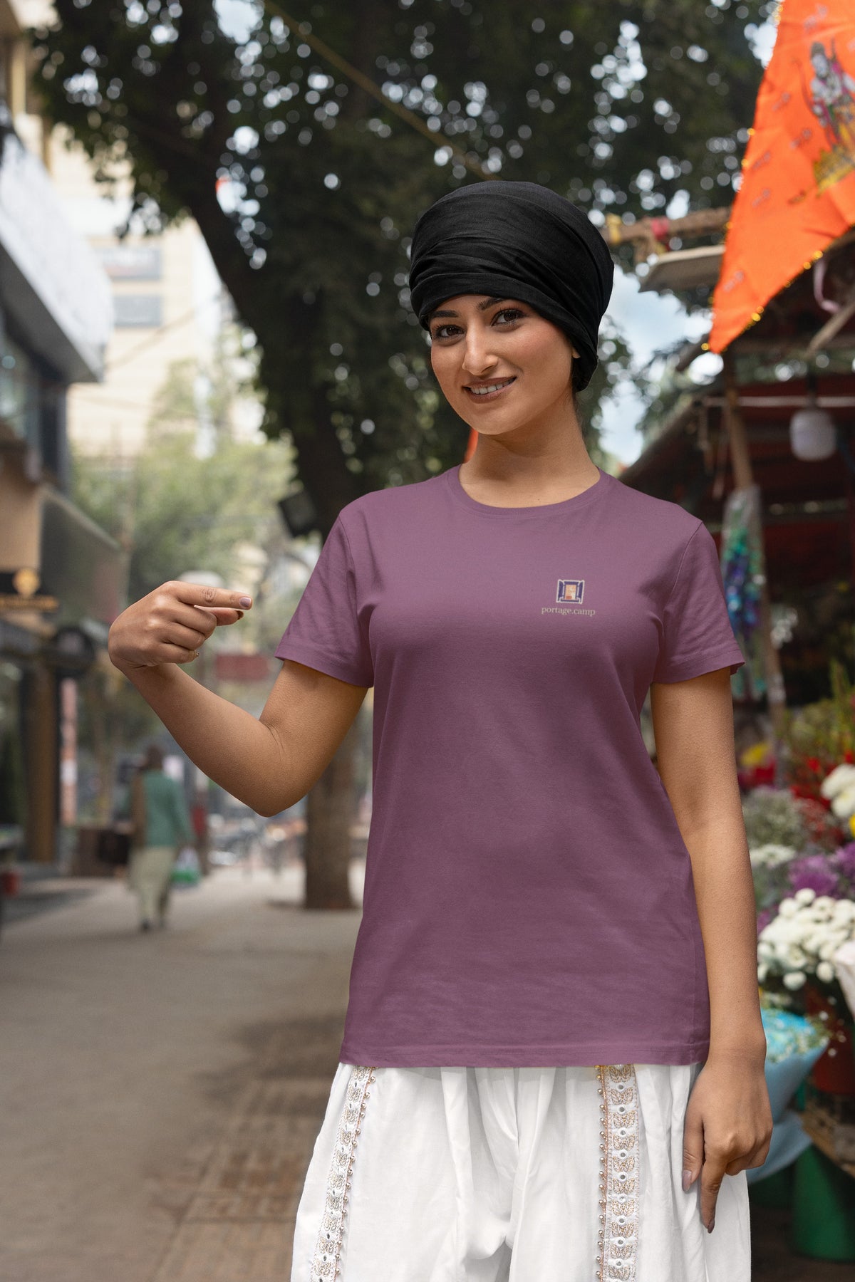 Open Late Garment-Dyed Tee in Berry, worn by a woman in a turban by a flower market, with the Open Late logo and portage.camp on the chest. Digital product mockup.